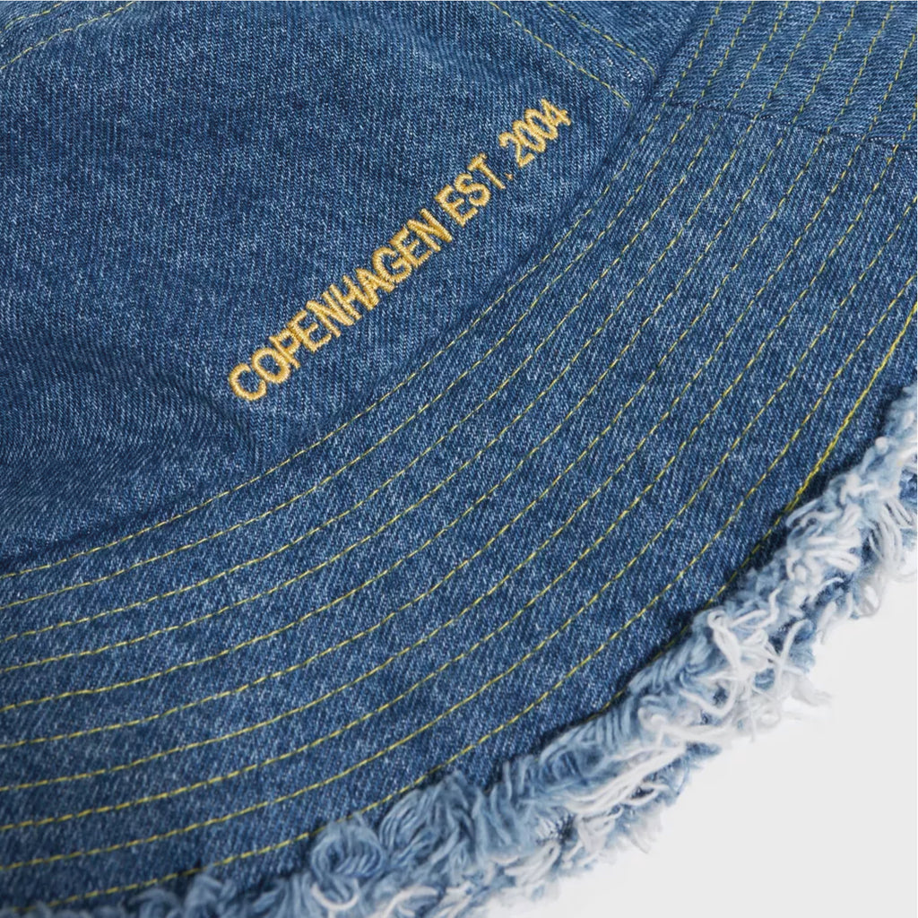 Jo And Co Beck Sondergaard Coronet Blue Denima Bucket Hat_Becksöndergaard Denima Bucket Hat in denim, featuring a raw edge and a yellow text detail.
