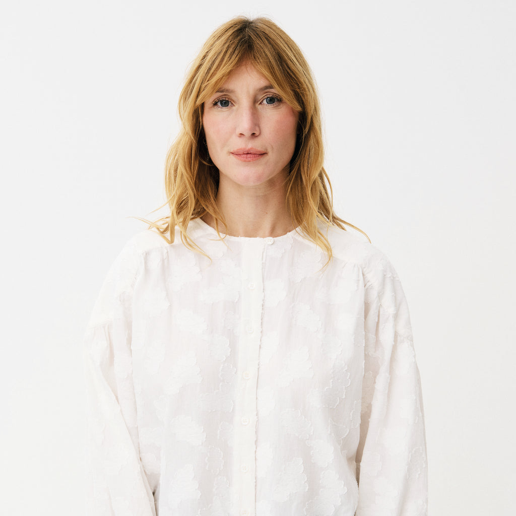 White blouse with cloud-like embroidery, button front, rounded neckline, slightly puffed sleeves with buttoned-cuffs and a gathered yoke at the back. 
Maison Anana White Aniella Blouse - Jo And Co Maison Anana White Aniella Blouse - Maison Anana